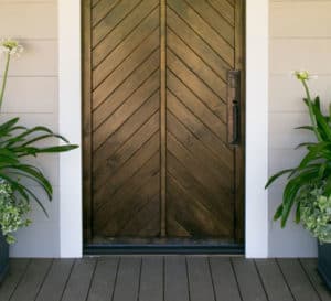 Beautiful chevron-patterned wooden doorway flanked by Queen Mum Agapanthus on a brick entryway at Southern Living Idea House