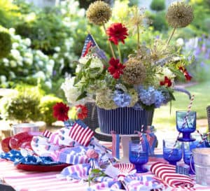 7月4日的餐桌包括一束Agapanthus和红色花朵，红色格子桌布，红色盘子和蓝色餐具