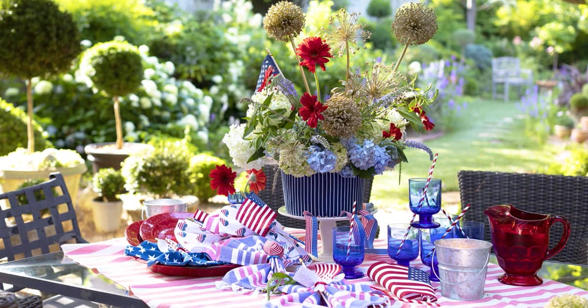 7月4日的餐桌包括一束Agapanthus和红色花朵，红色格子桌布，红色盘子和蓝色餐具