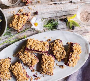 黑莓燕麦碎条放在白色椭圆形盘子上，放在肉铺上，碗里是新鲜的黑莓和黑莓花