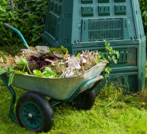 绿色的手推车装满了厨房和院子里的垃圾，停在堆肥箱旁边