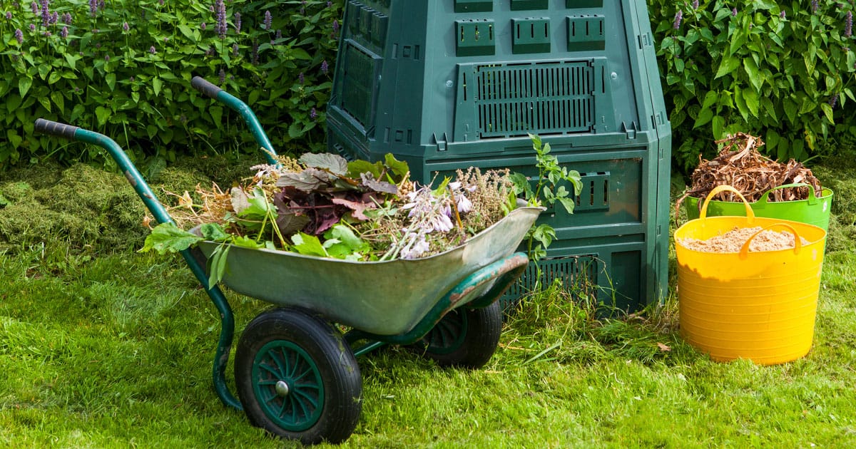 一辆装满厨房和院子废料的绿色手推车停在堆肥箱旁边